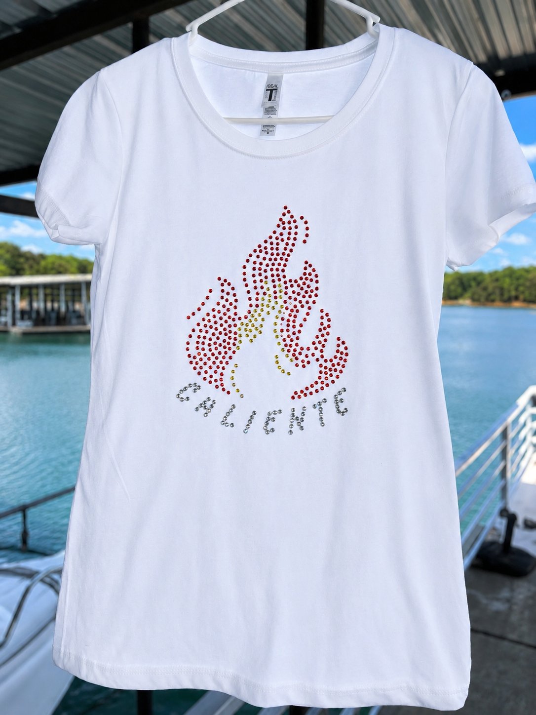 Camiseta blanca ajustada para mujer con diseño de fuego en rhinestones rojos y amarillos y la palabra “Caliente”.