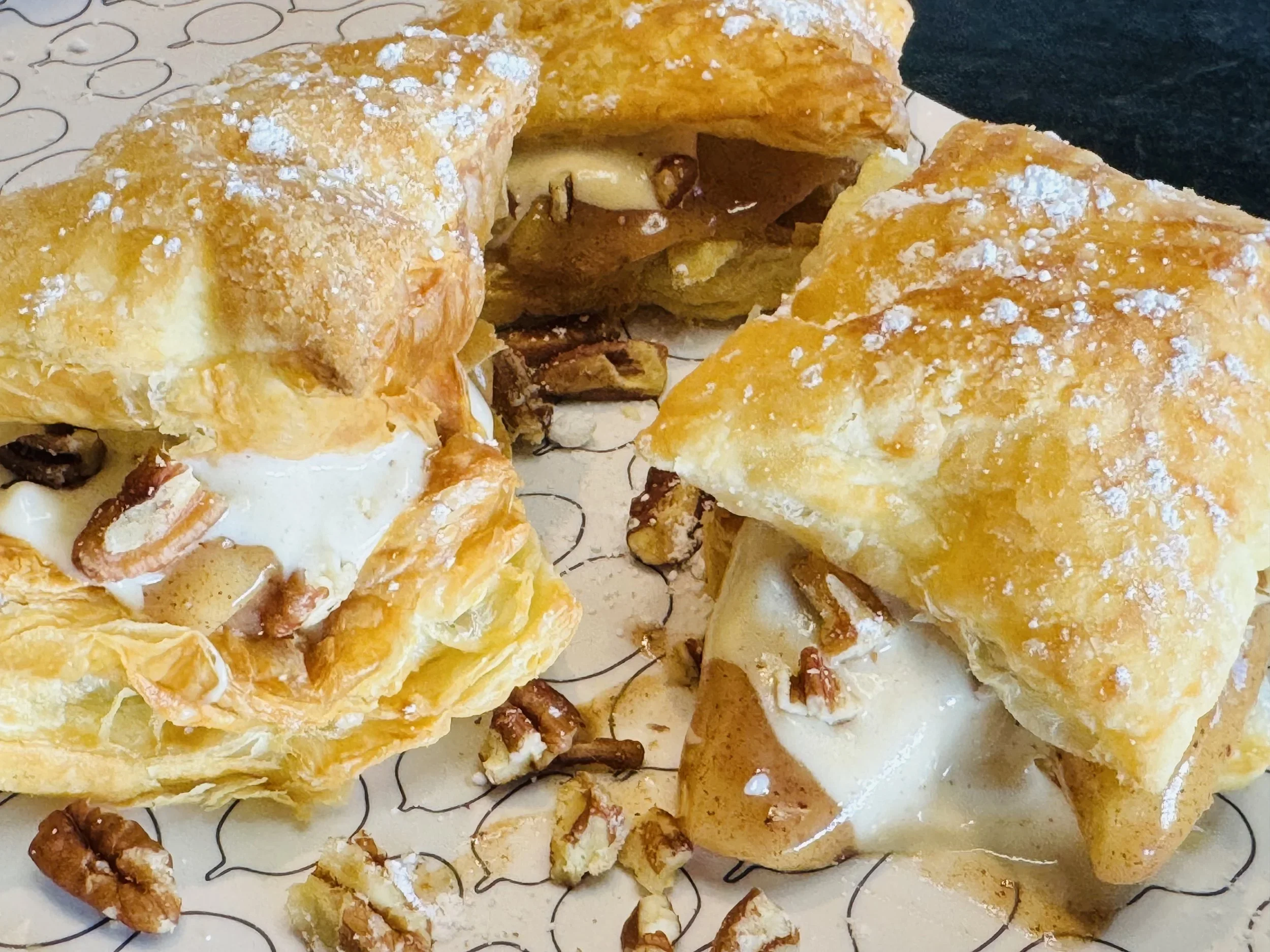 Flaky apple pie pastries filled with warm apples, cream topping, pecans, and powdered sugar
