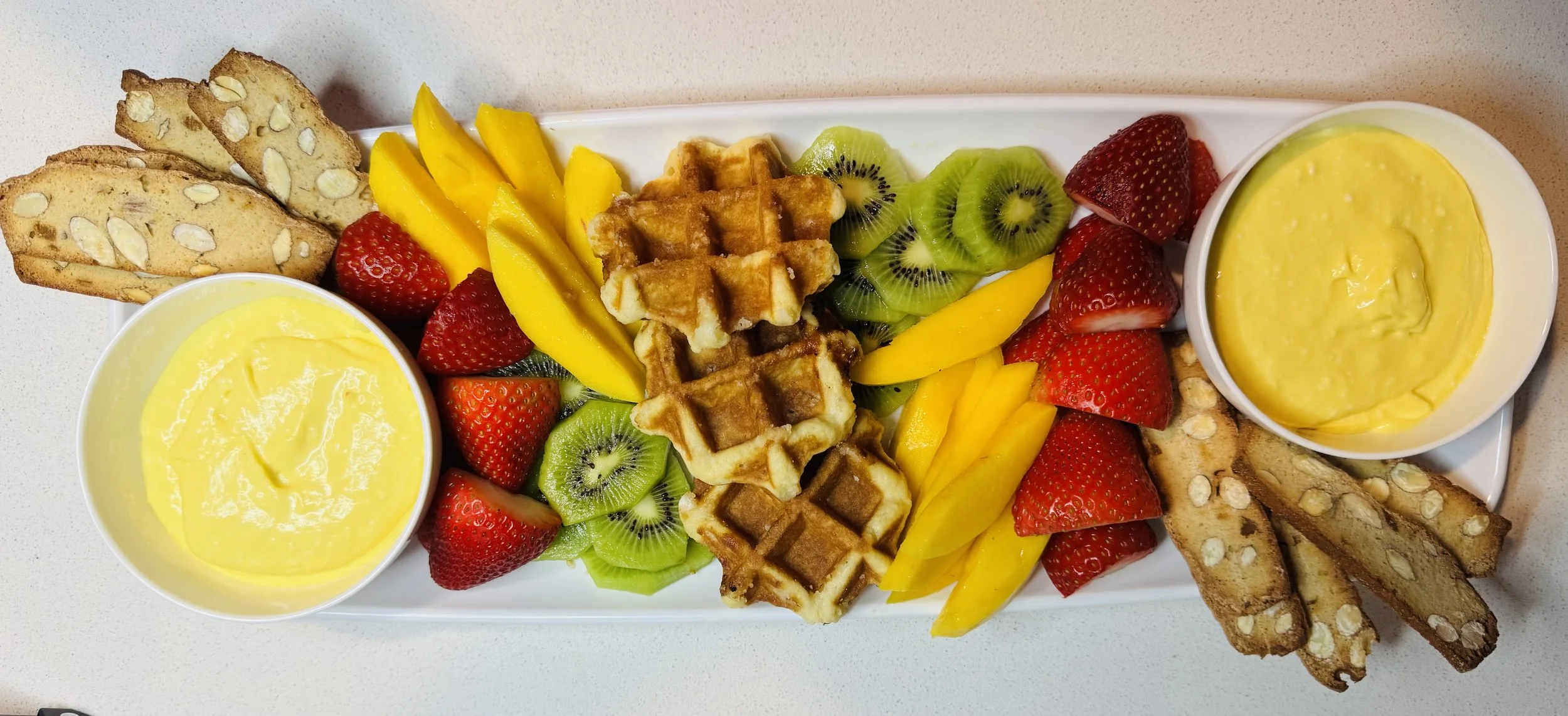 Creamy mango dip served with fresh fruit, waffle pieces, and wafer cookies