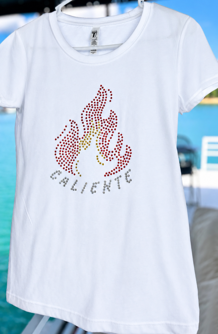 Camiseta blanca ajustada para mujer con diseño de fuego en rhinestones rojos y amarillos y la palabra “Caliente”.