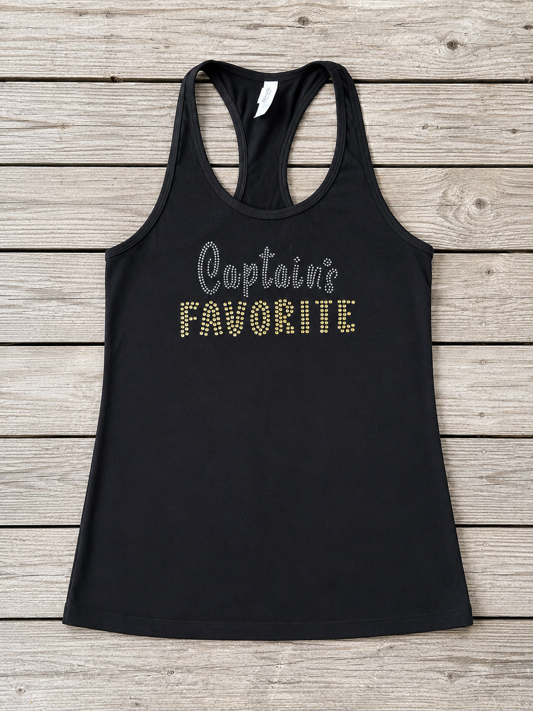 Black racerback tank top featuring silver and gold rhinestone lettering that reads "Captain's Favorite," displayed on a rustic wood background.