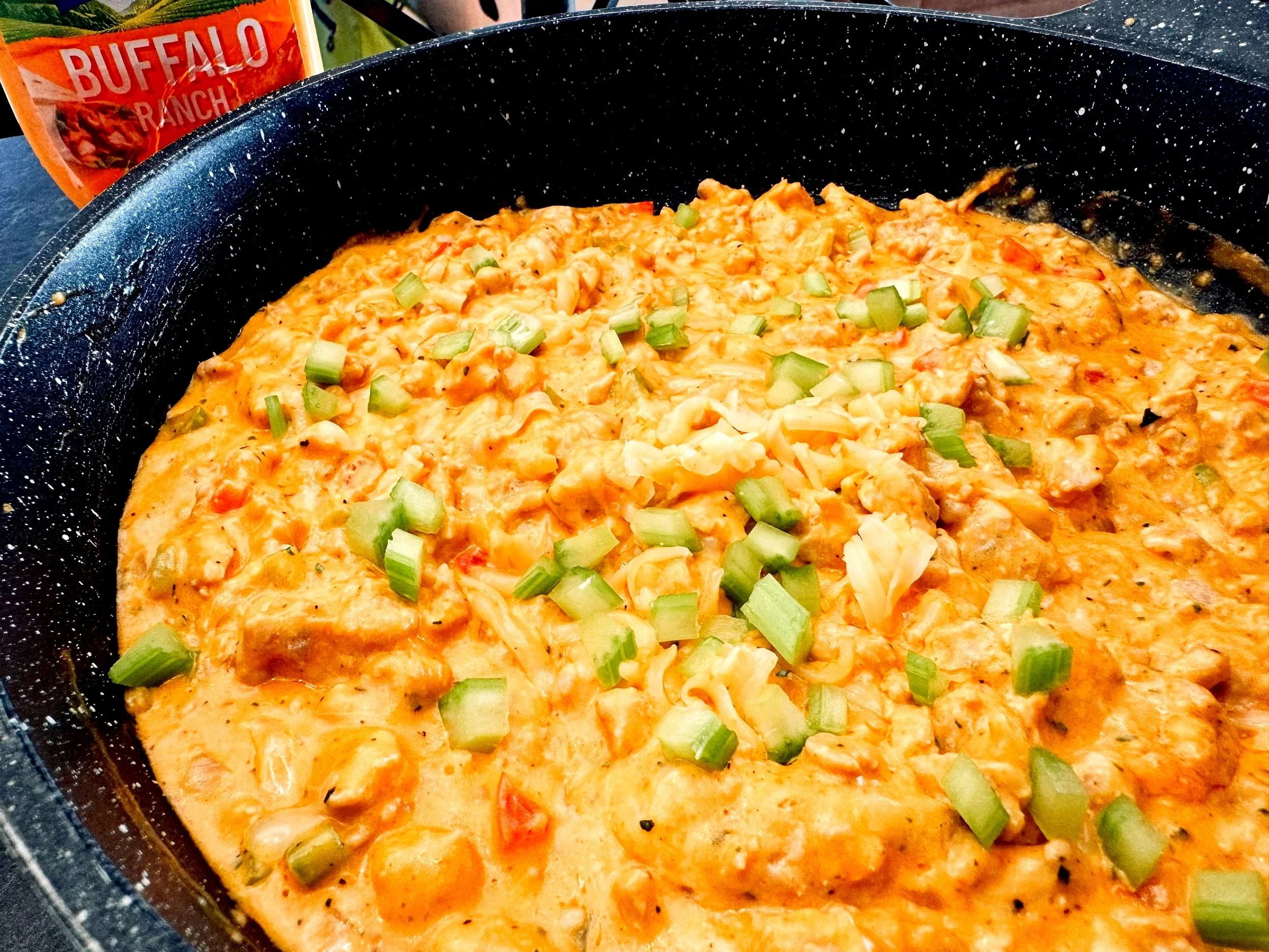 Creamy buffalo ranch chicken dip topped with green onions in a skillet