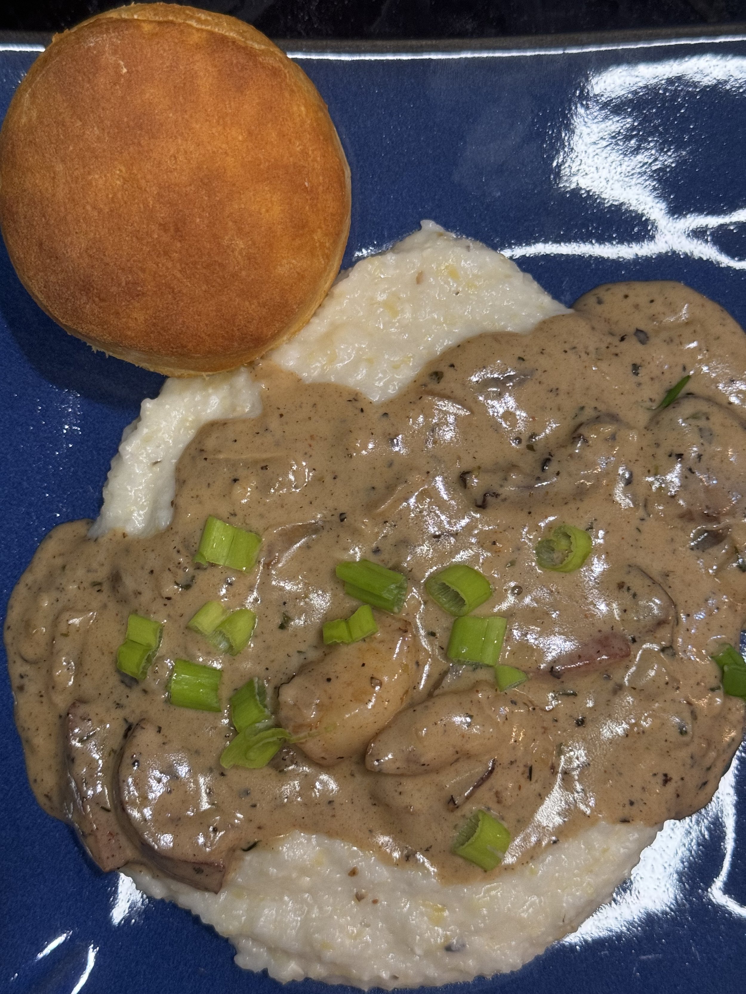 Shrimp and Sausage Gravy Over Grits with a Biscuit on a plate