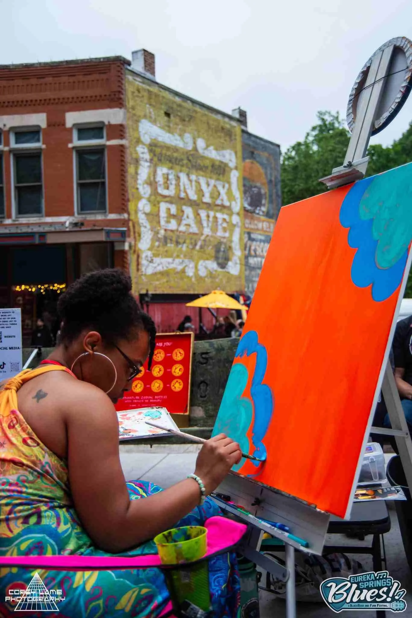 Artist doing a live artist painting at a music festival. She is in the process of creating a large, vibrant, abstract canvas painting.