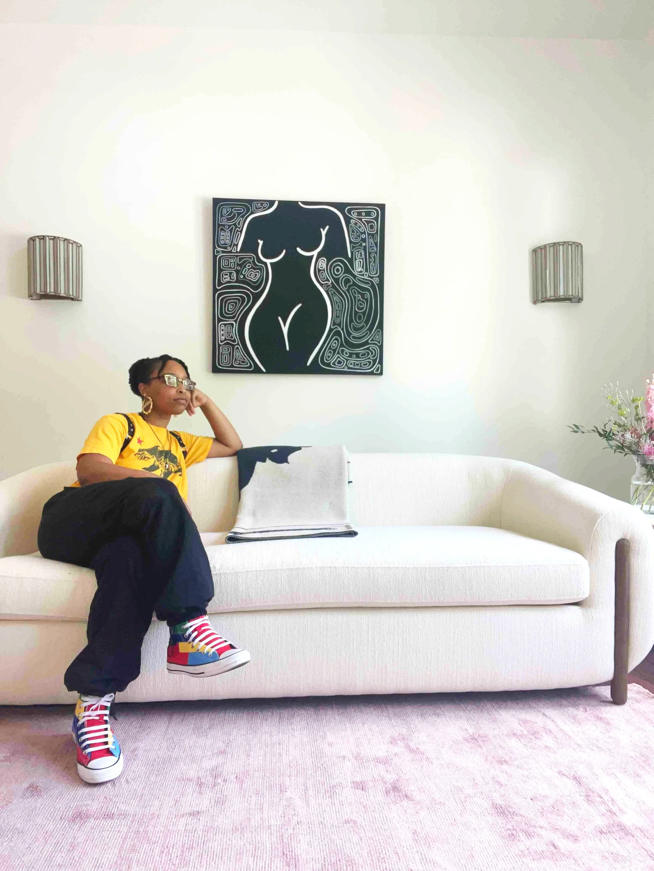 Artist sitting on a couch in front of an abstract wall art painting hanging on a wall in a living room area.