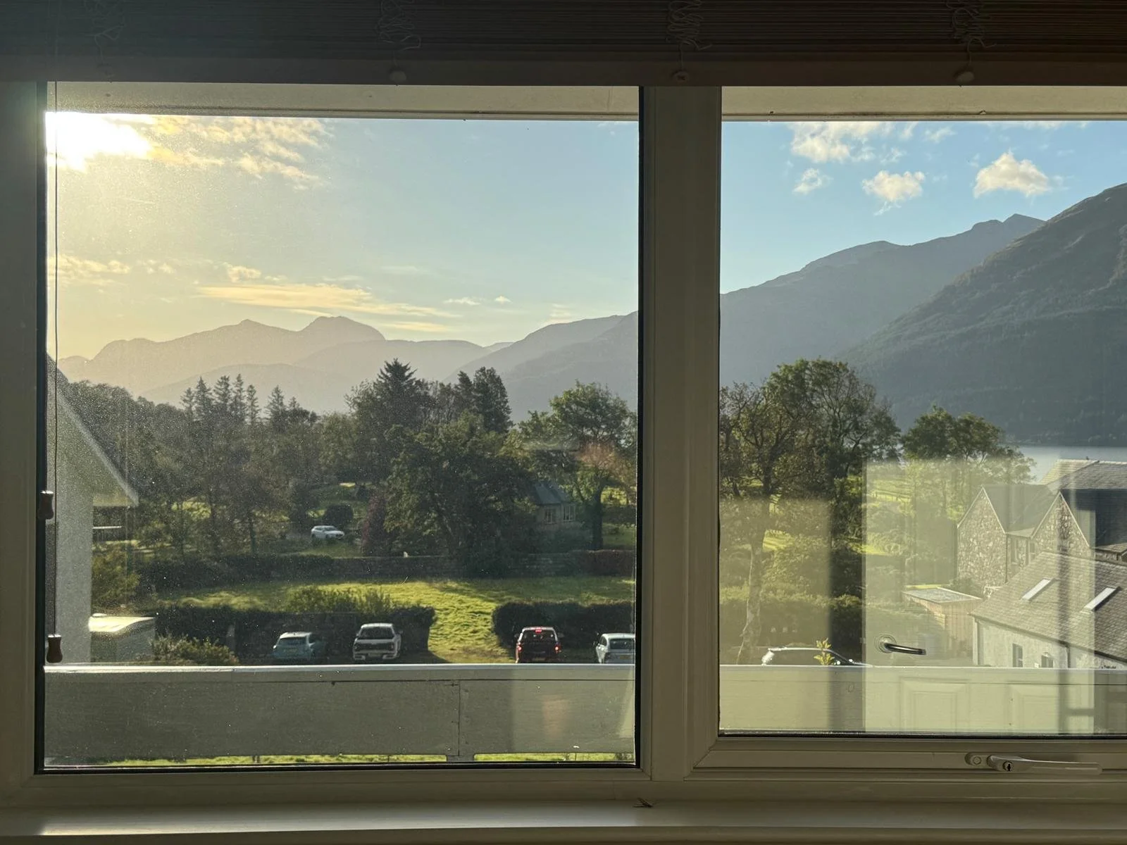 A scenic view of mountains, trees, and a parking lot through a large window with part of the window frame visible.