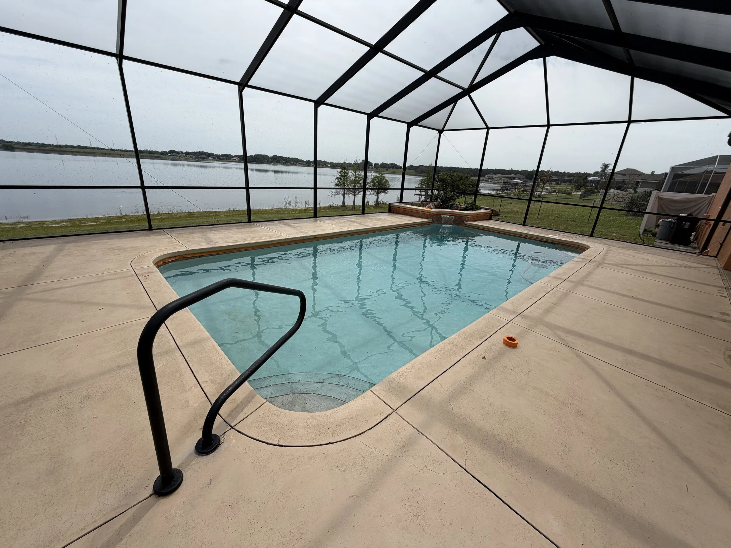 Pressure washing a screened pool enclosure and lanai near a lake in Polk County, FLPerson wearing blue jeans and green rubber boots pressure washing outdoor pavement.