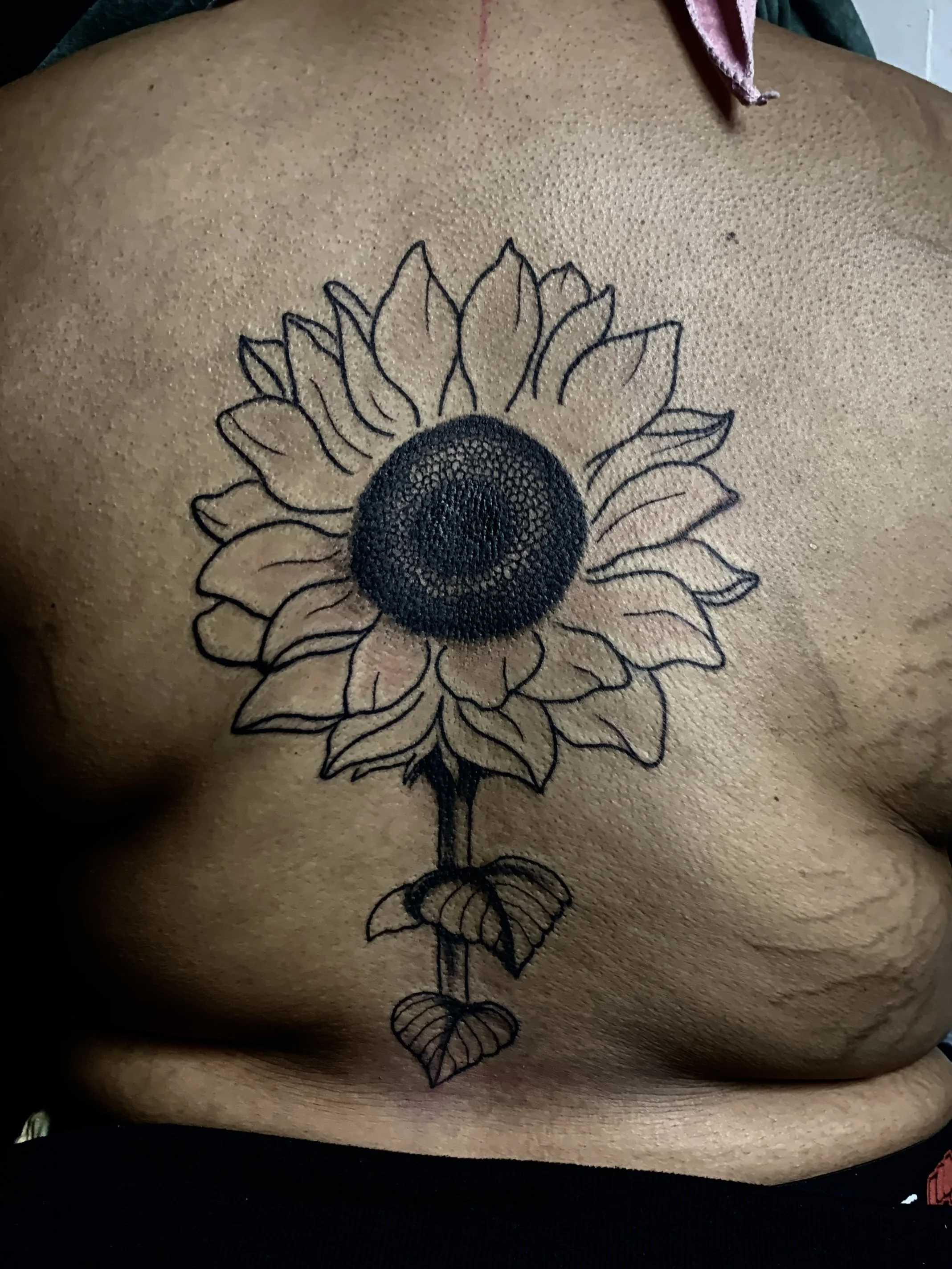 A sunflower black and grey tattoo with back placement.