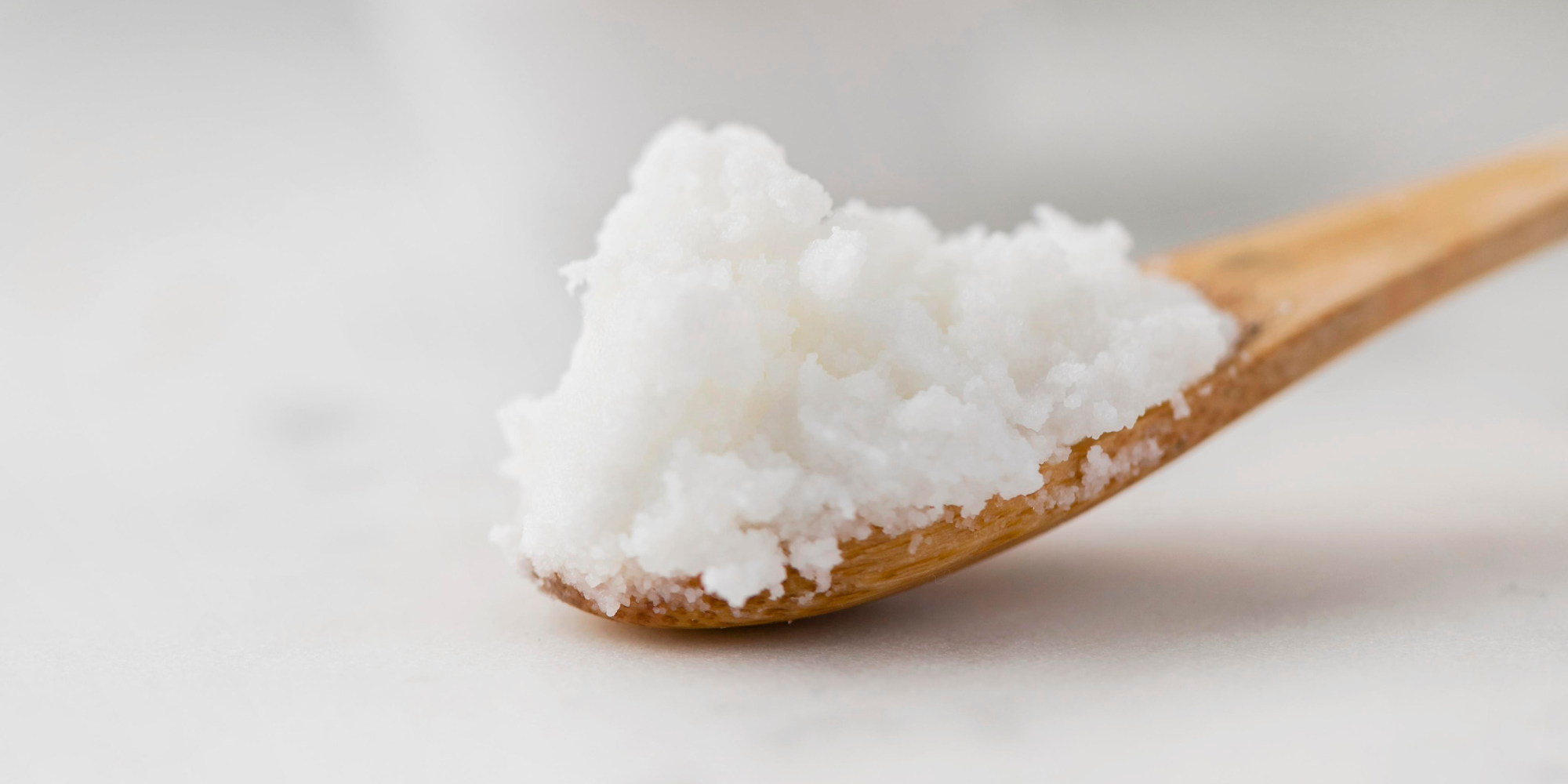 Wooden spoon with coconut oil against a light background.