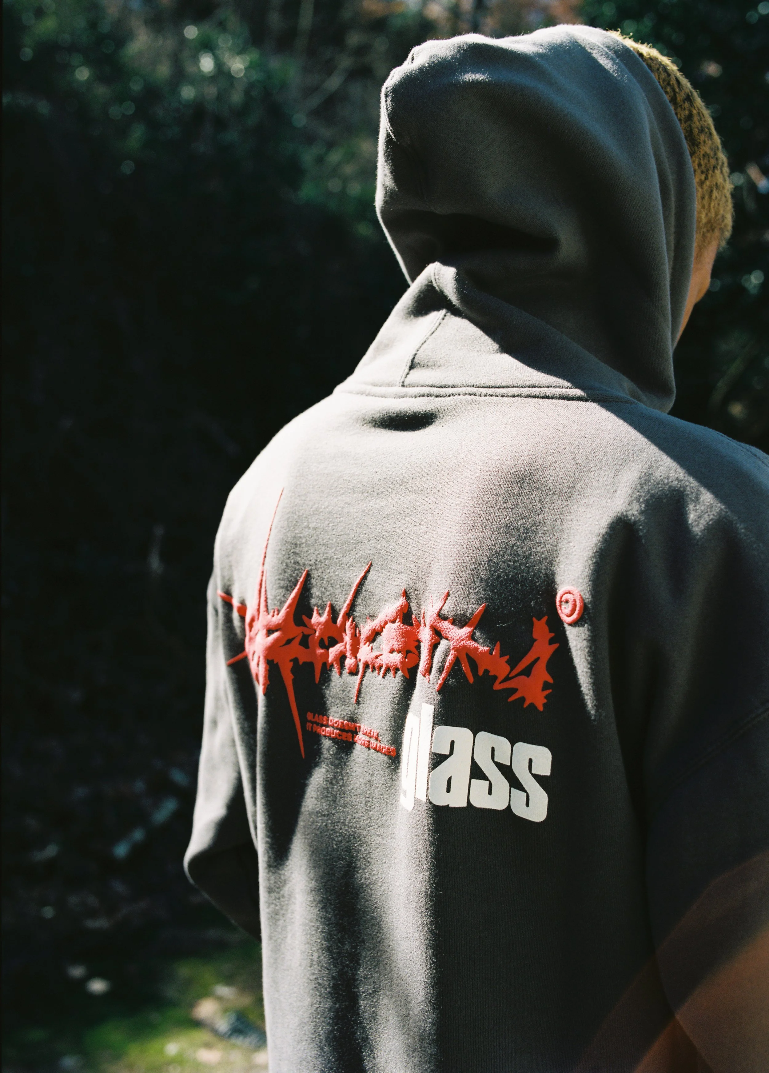 Back of a person wearing a gray hoodie with red and white graphic text and design on the back outside.