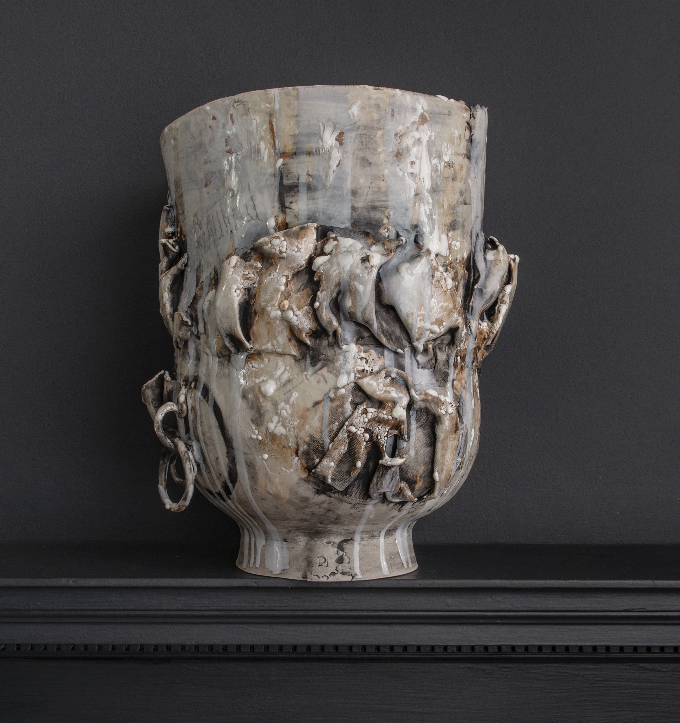 Close-up of a ceramic or stone sculpture with an abstract, textured surface in neutral tones, placed on a black shelf against a dark background.