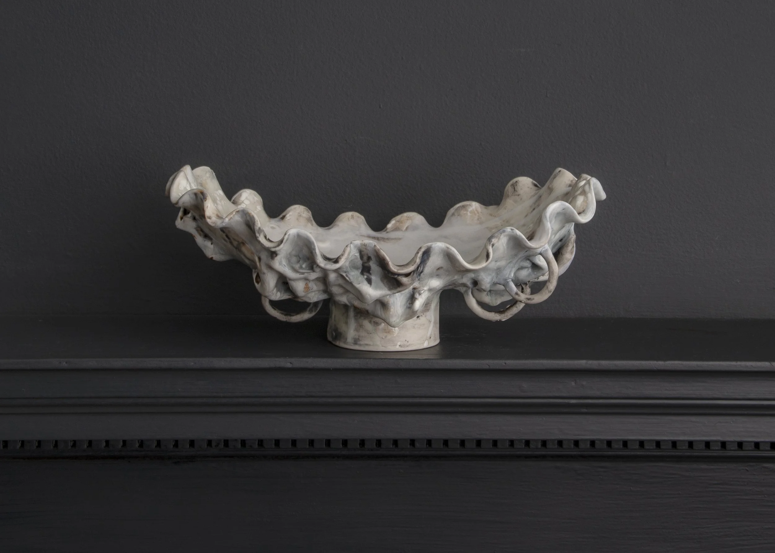 White ceramic shell-shaped bowl on black surface against a gray background.