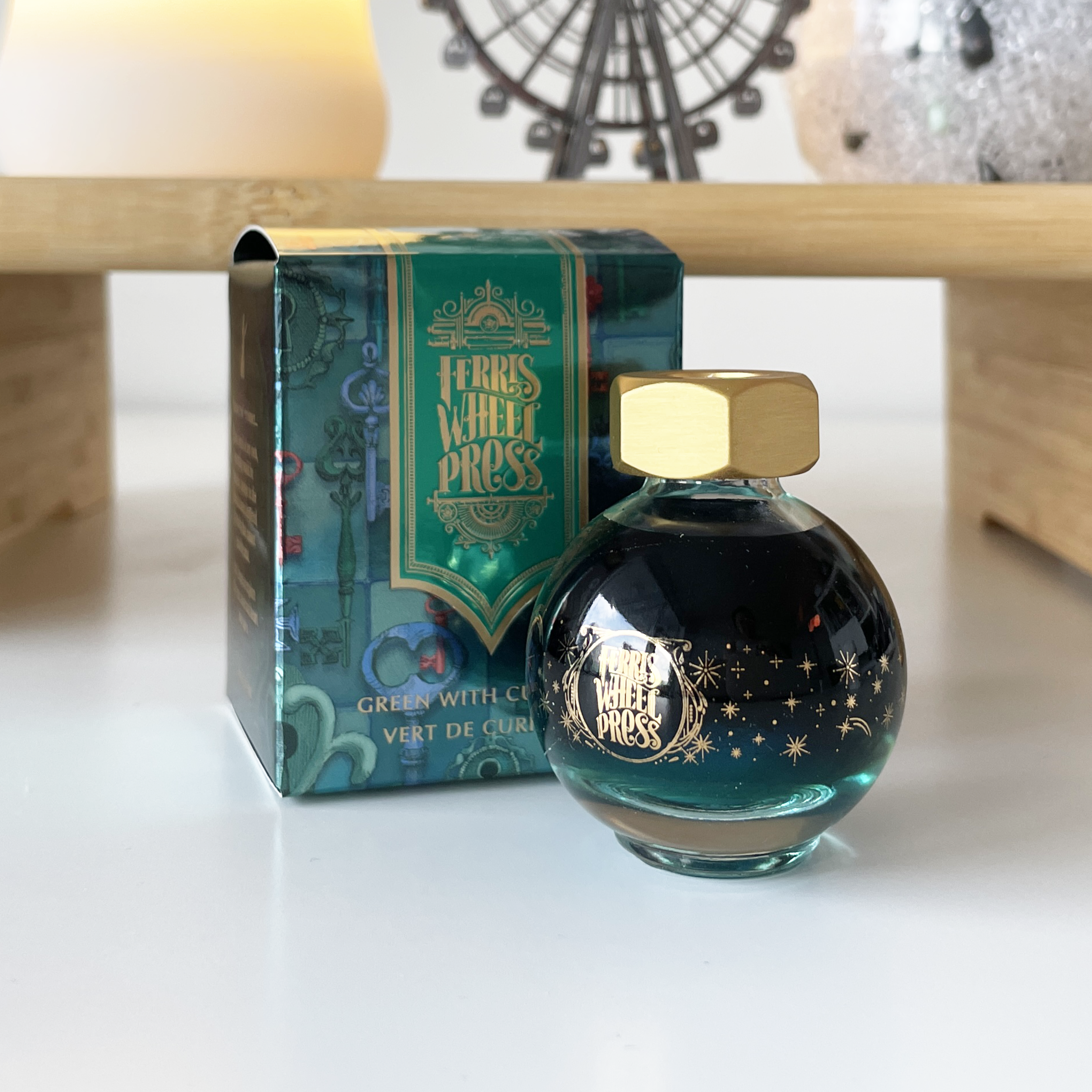 A photo of the round globe, 20mL bottle of Ferris Wheel Press 'Green With Curiosity' in front of the packaging.