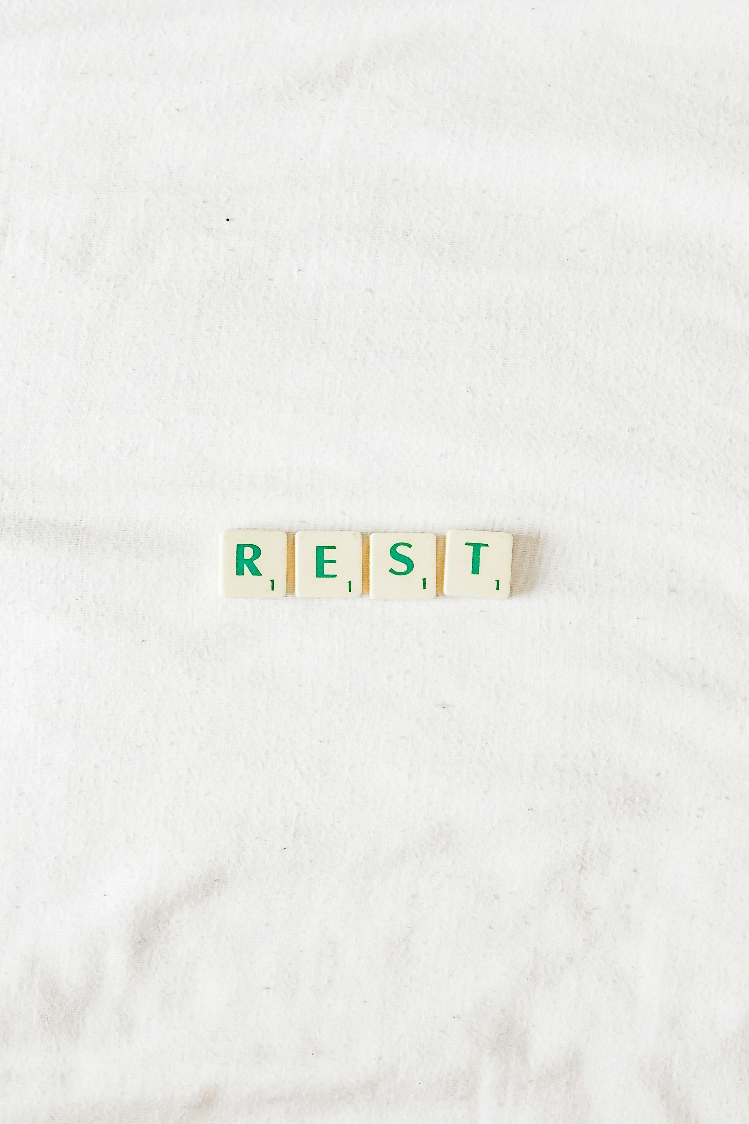 Scrabble tiles spelling the word REST arranged on a white textured background.