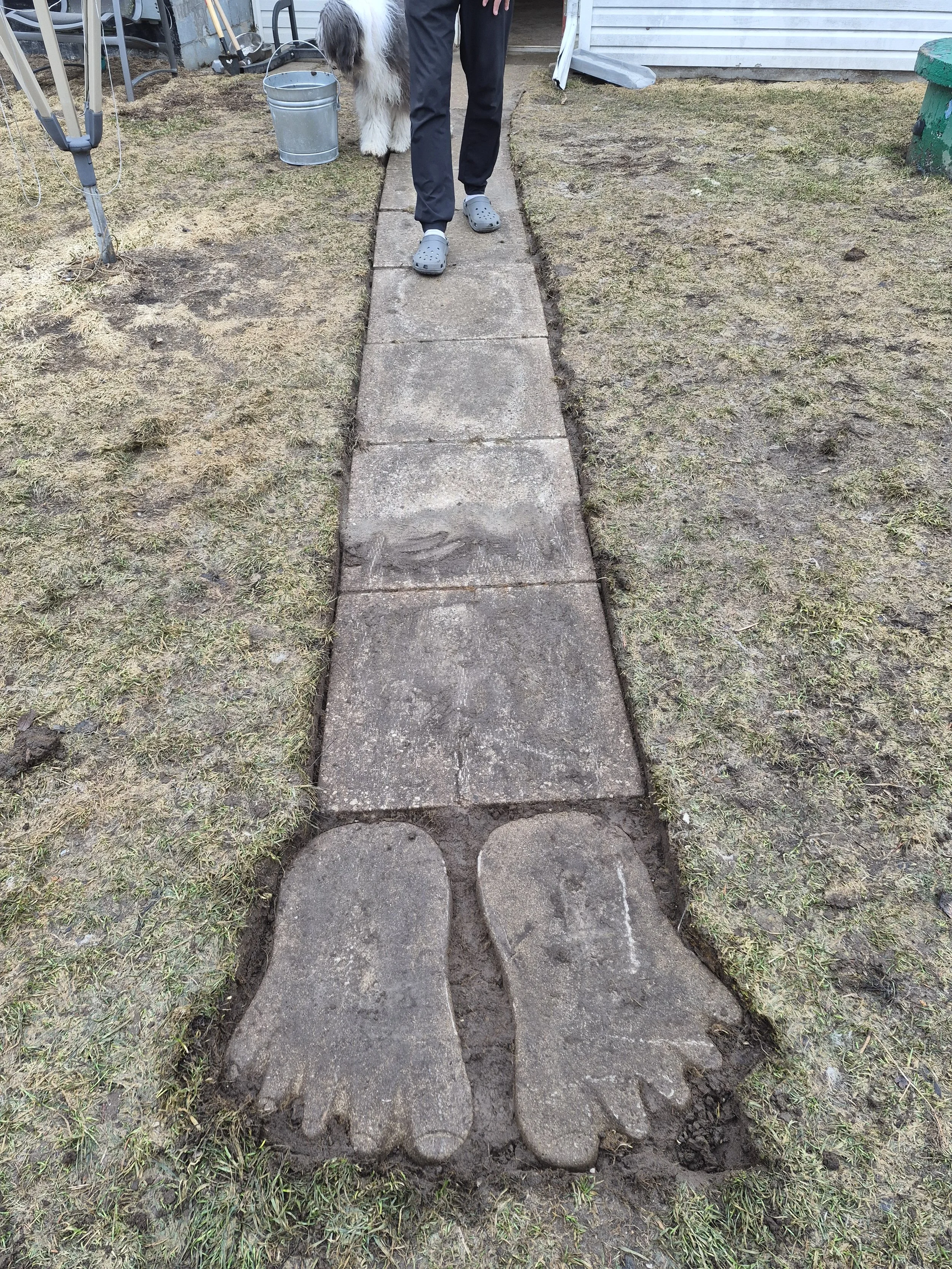 A stone walkway in grass with stone feet at the end