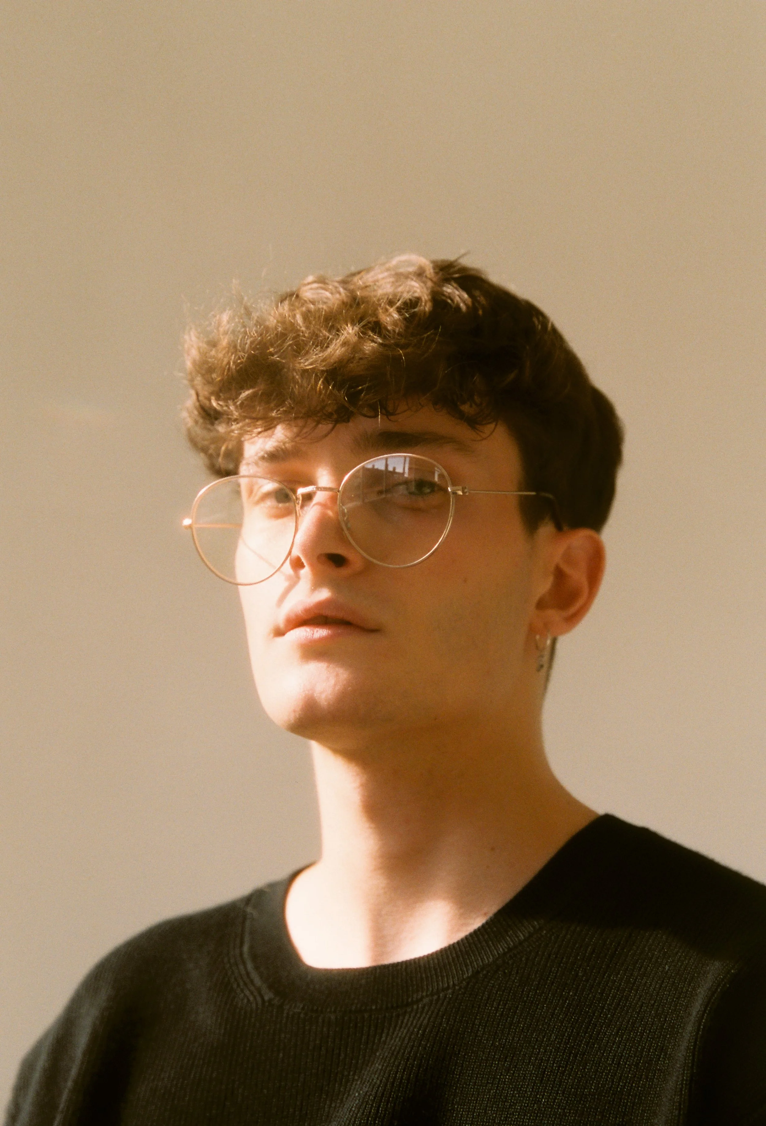Retrato fotográfico analógico de un joven guapo y estiloso con gafas sentado en una silla de madera.
