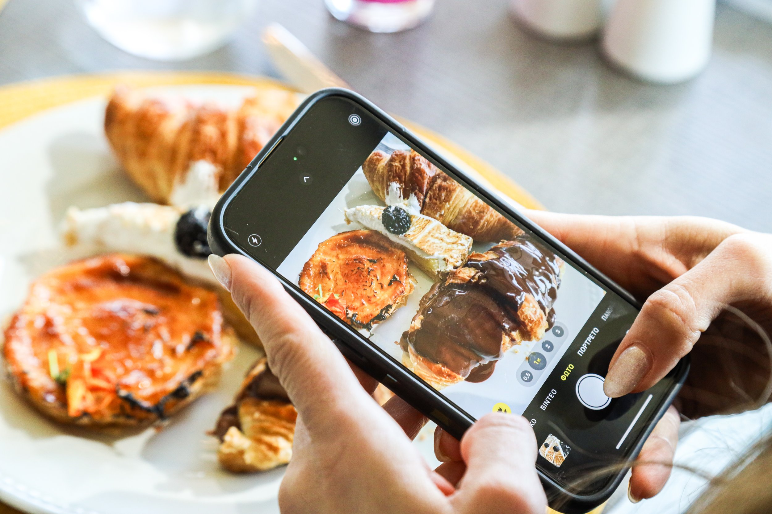 Person taking a photo of assorted pastries on a plate with a smartphone.