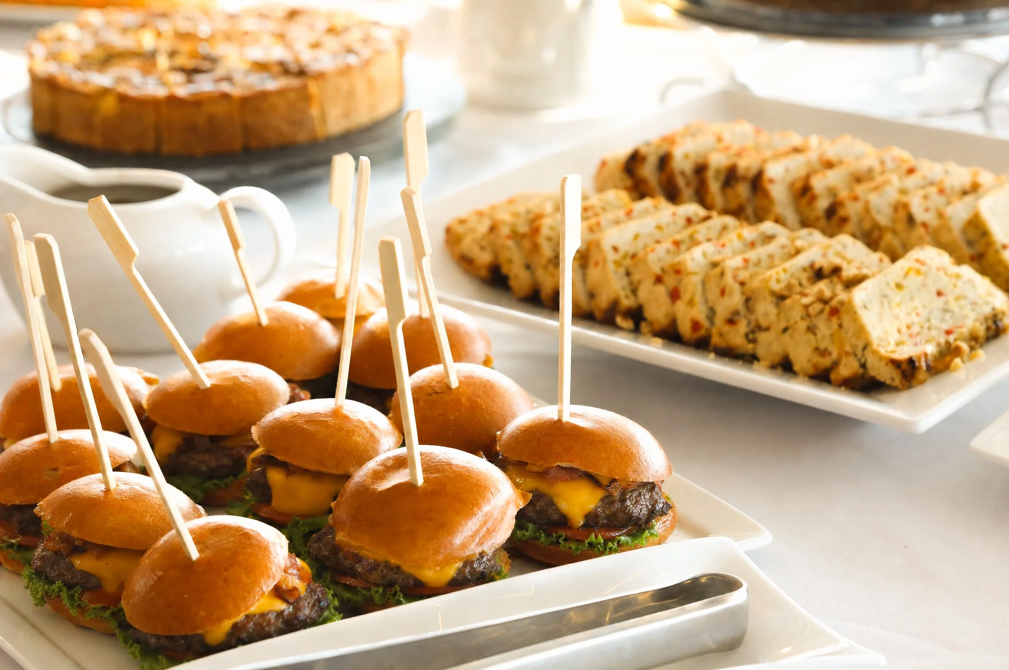 Mini cheeseburgers with lettuce and cheese on small buns arranged on a white tray.