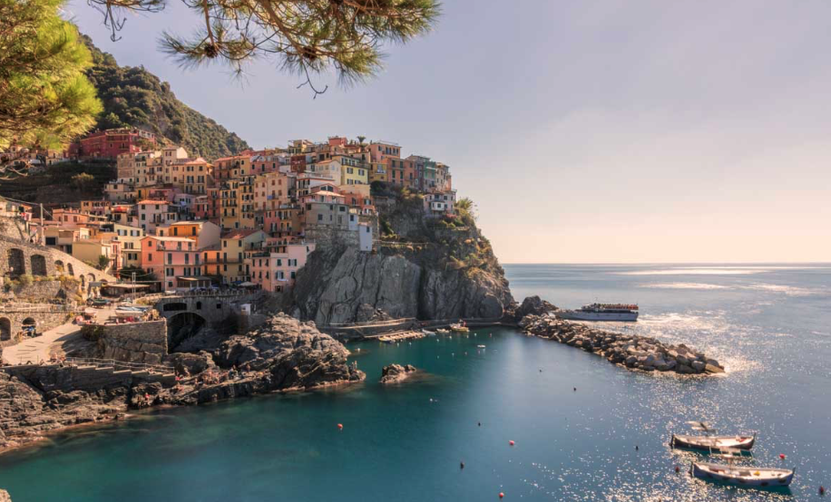 Manarola with colorful houses perched on rocky cliffs overlooking a small harbor with boats and the sea on a sunny day in a coastal town.
