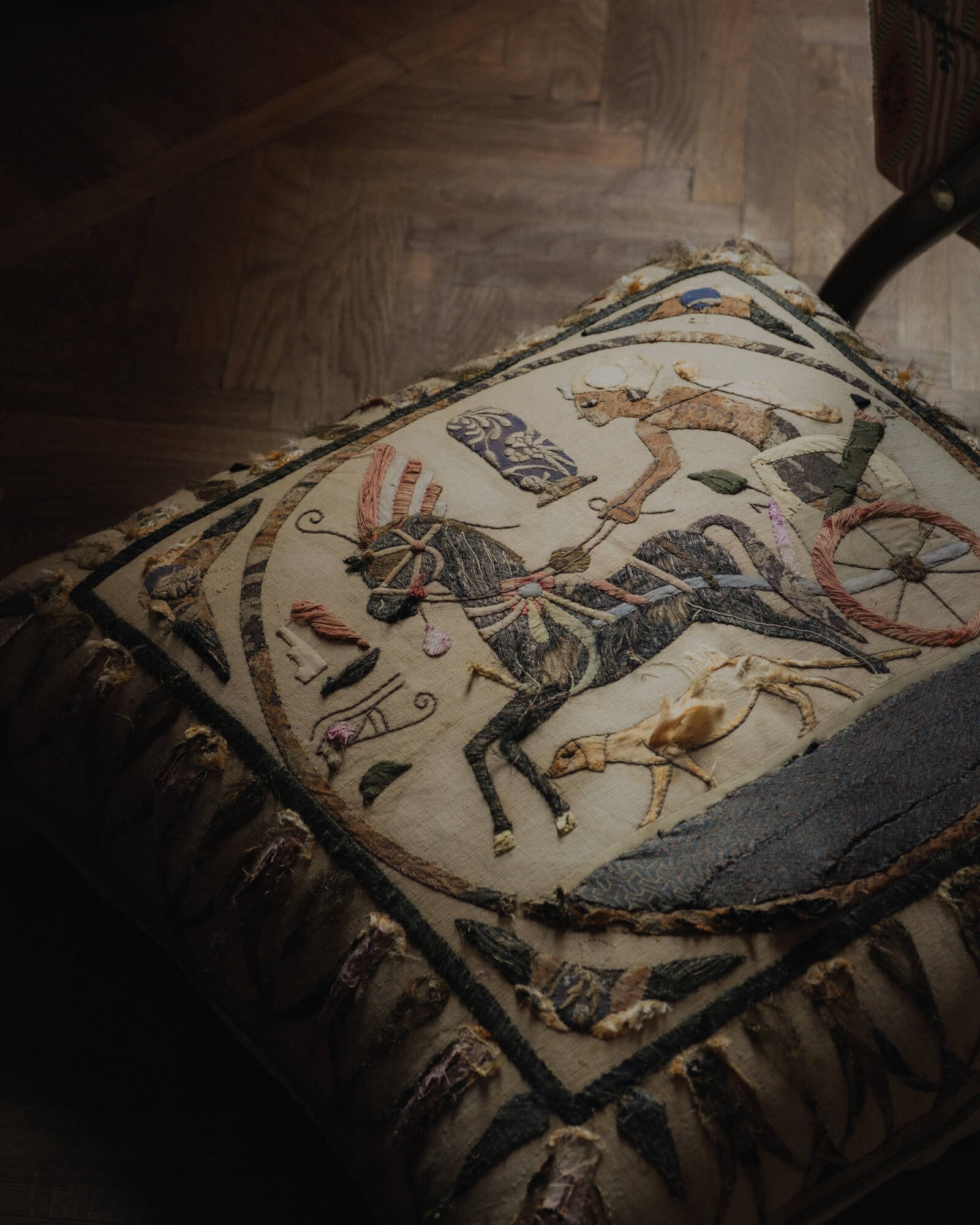 Close-up of an embroidered fabric with a depiction of a knight on a horse, featuring floral motifs and intricate detailing, resting on a wooden surface.