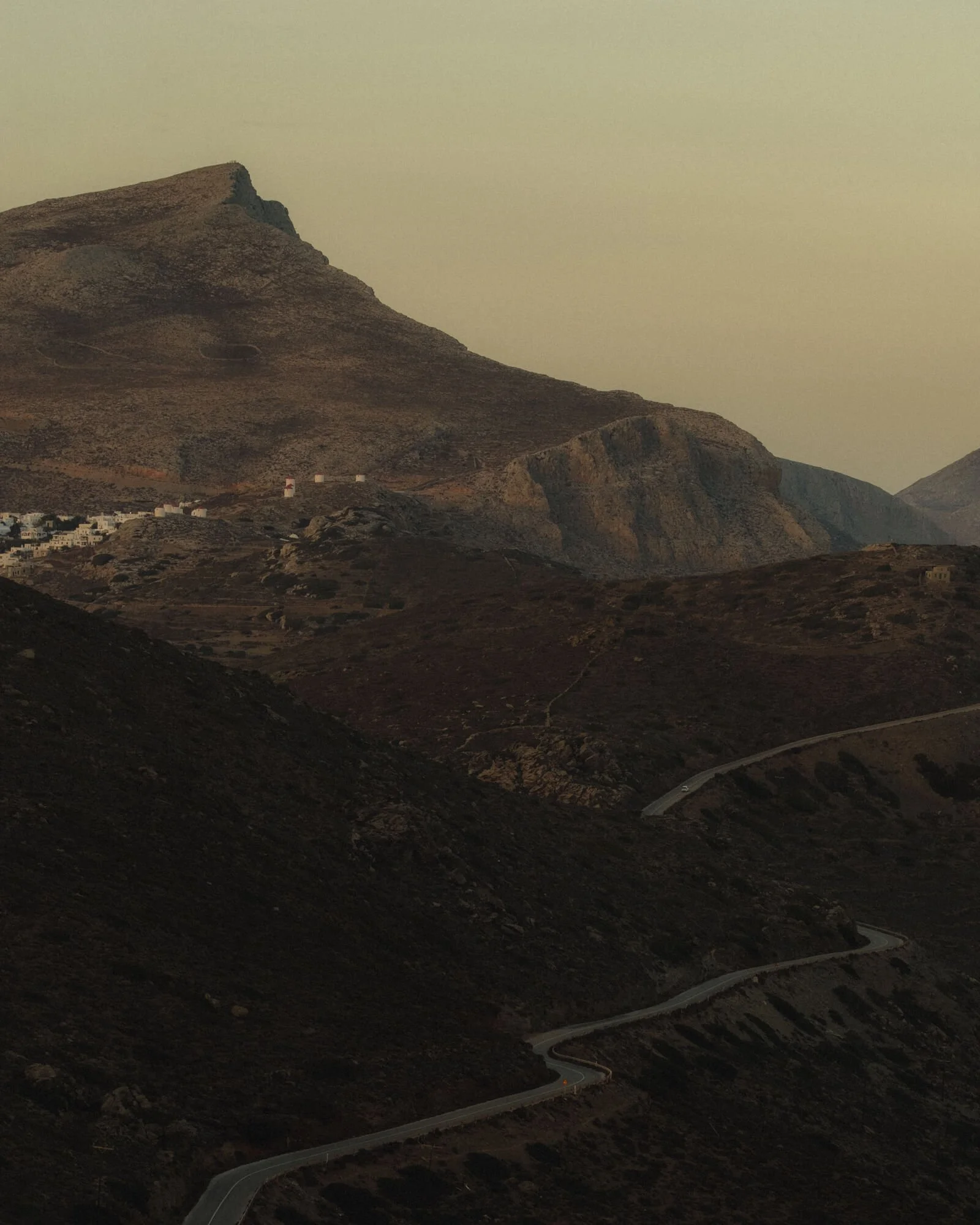 A winding road through a mountainous desert landscape with rocky hills and sparse vegetation under a hazy sky.