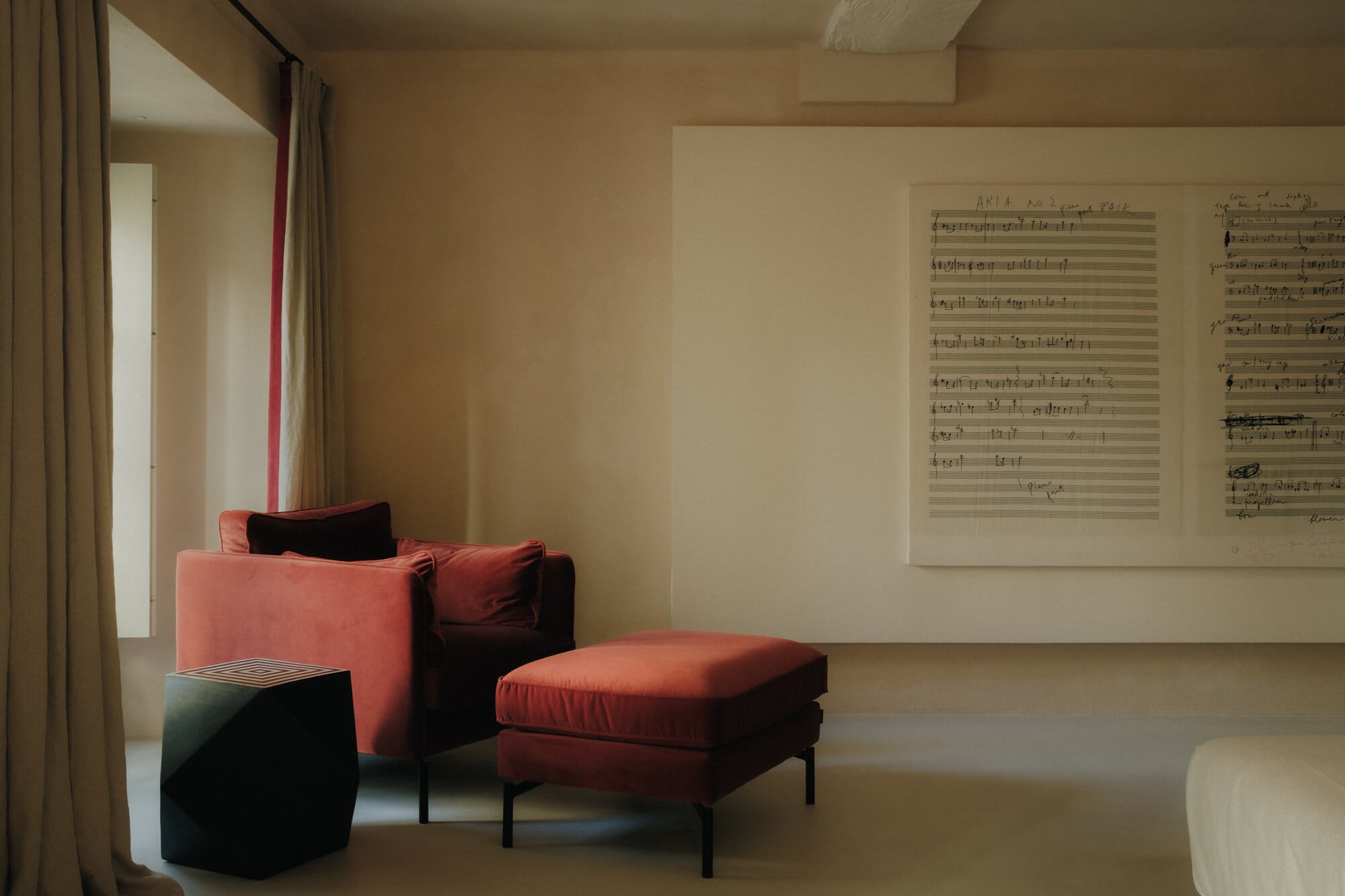 A cozy living room with pink upholstered chairs, a matching ottoman, a side table, and a wall-mounted sheet music display.