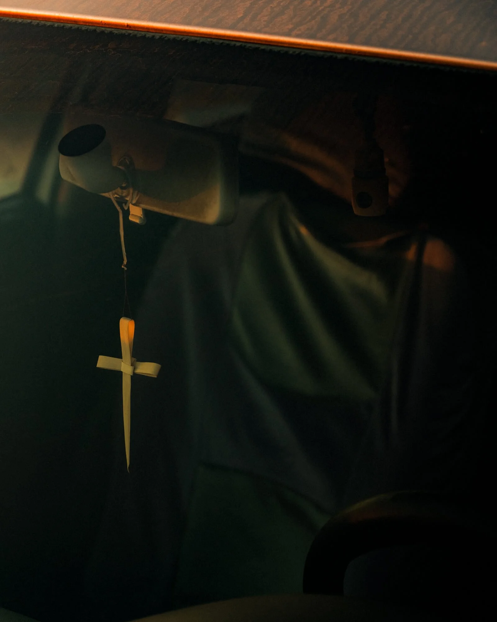 The image shows the interior of a car, focusing on the rearview mirror and a hanging decoration with a cross.