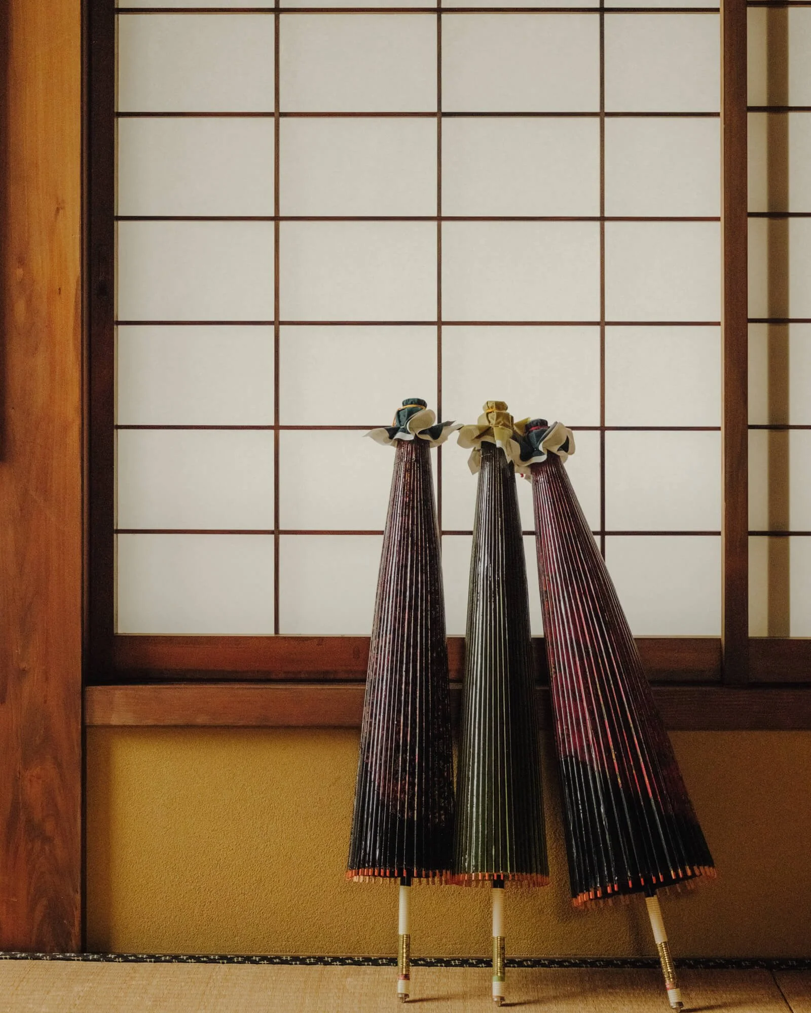 Three Japanese wagasa umbrellas with wooden handles leaning against a wall with shoji-style paper sliding doors.