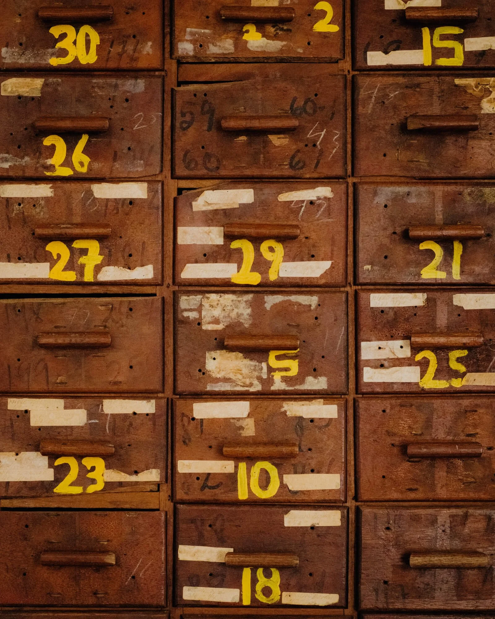 Multiple old wooden drawers labeled with yellow numbers from 1 to 30, some drawers are missing labels, showing signs of wear and tear.