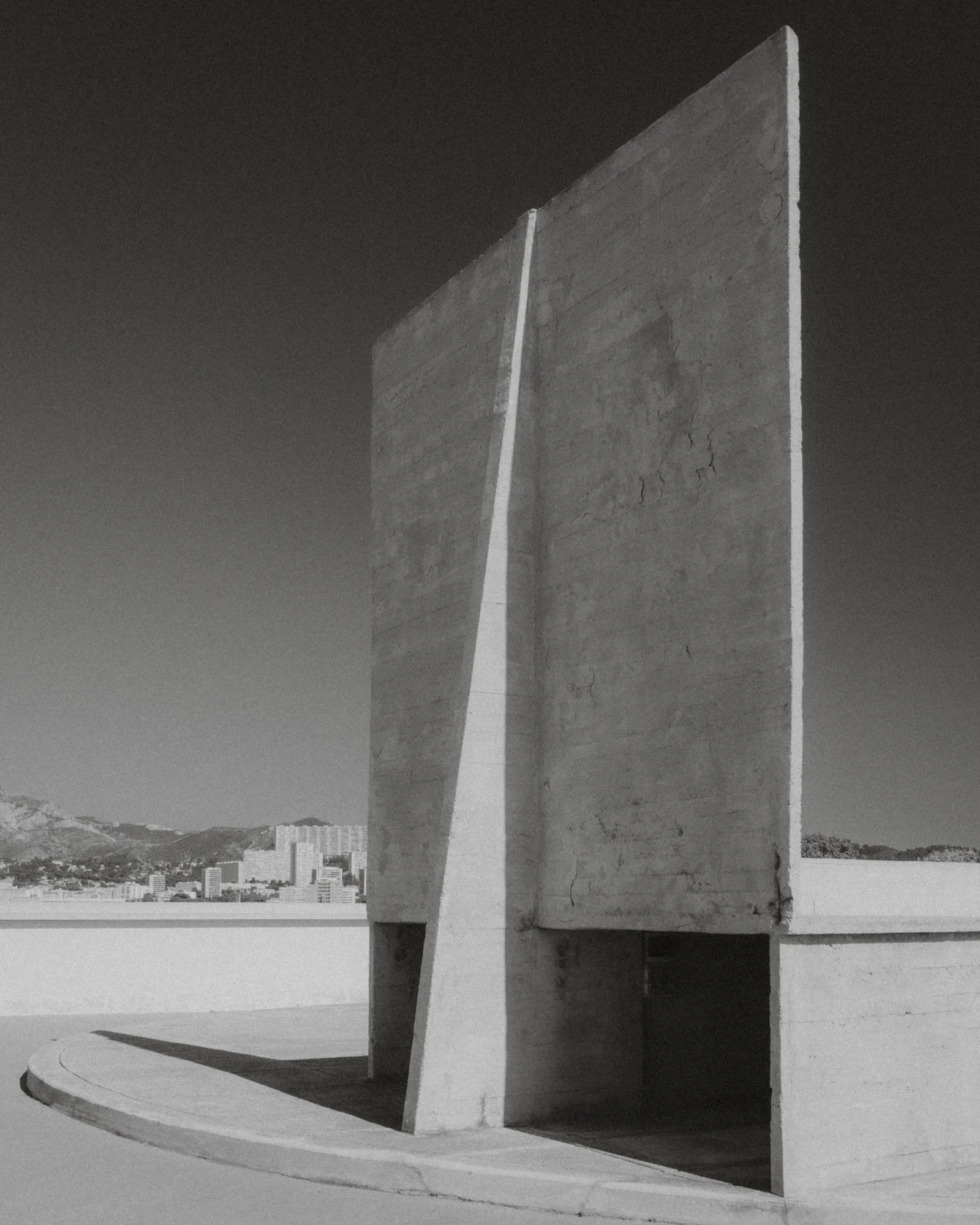 Black and white photo of the United States Holocaust Memorial Museum building in Washington, D.C. with distinctive modern architecture, curved concrete, and city skyline in the background.