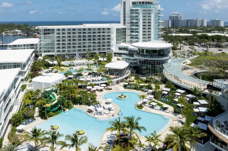 Lagoon-style pool at Pier Sixty-Six Resort, Fort Lauderdale, surrounded by palm trees, sun loungers and contemporary waterfront hotel towers by the marina.
