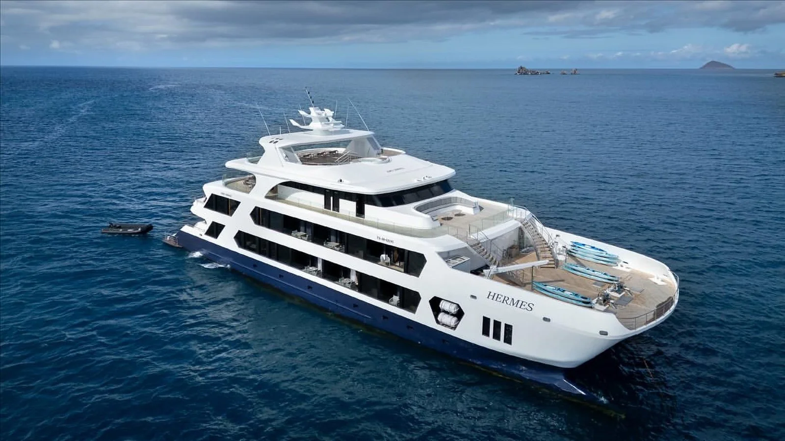 Luxury Hermes mega catamaran yacht anchored in the Galápagos, featuring multi-deck terraces, outdoor lounges, and ocean views under a clear blue sky.