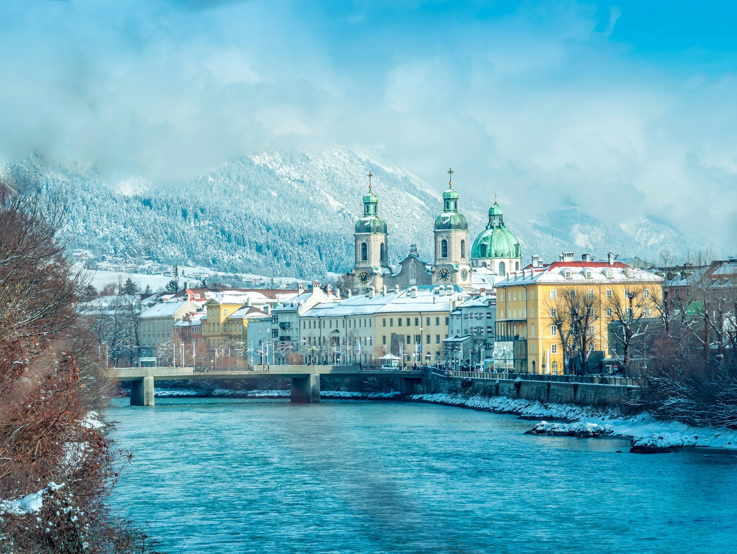 View of Innsbruck Old Town along the River Inn, with historic buildings and snow-dusted Alps in the background on a clear winter day