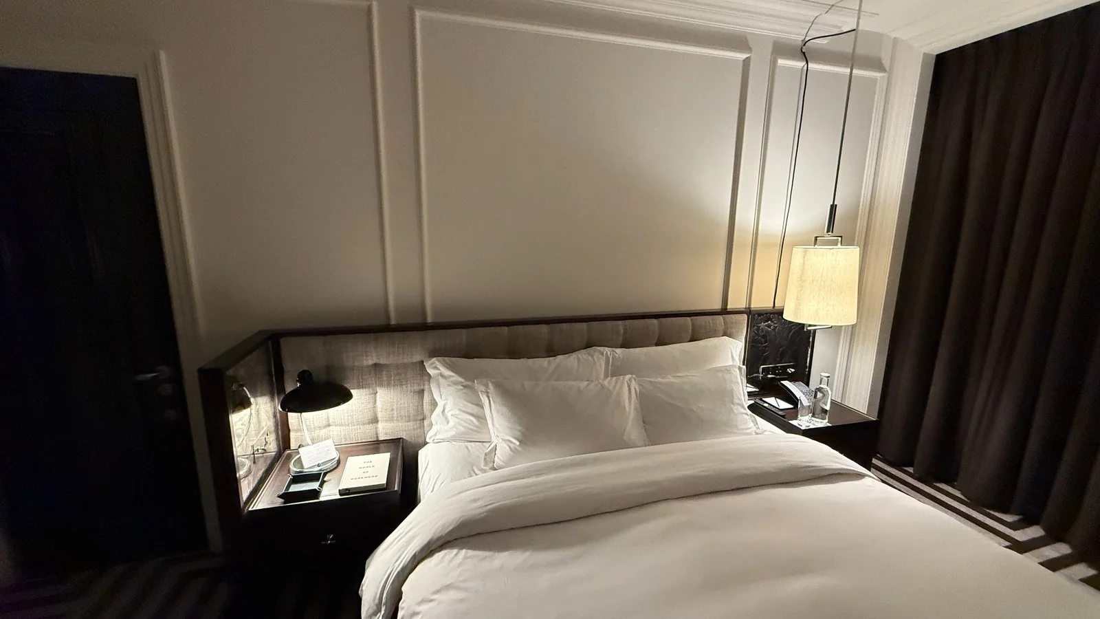 King bed with white linens and bedside lighting in a Rosewood London bedroom at night