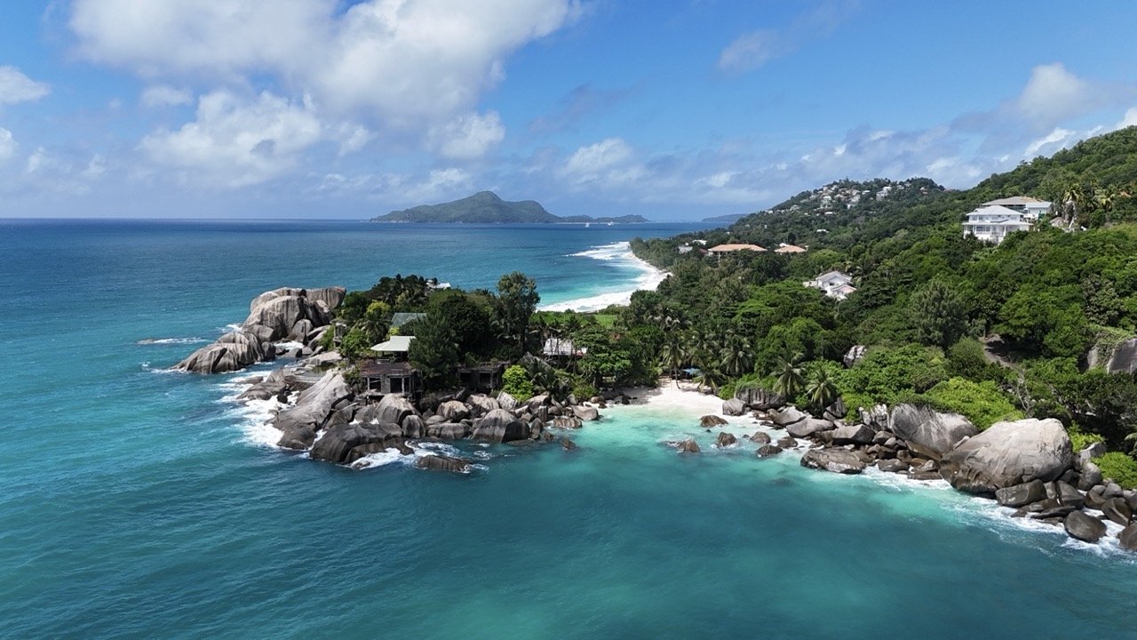 A breathtaking aerial view of Mahé Island, Seychelles, showcasing a rugged coastline with turquoise waters and lush greenery stretching along the shoreline.