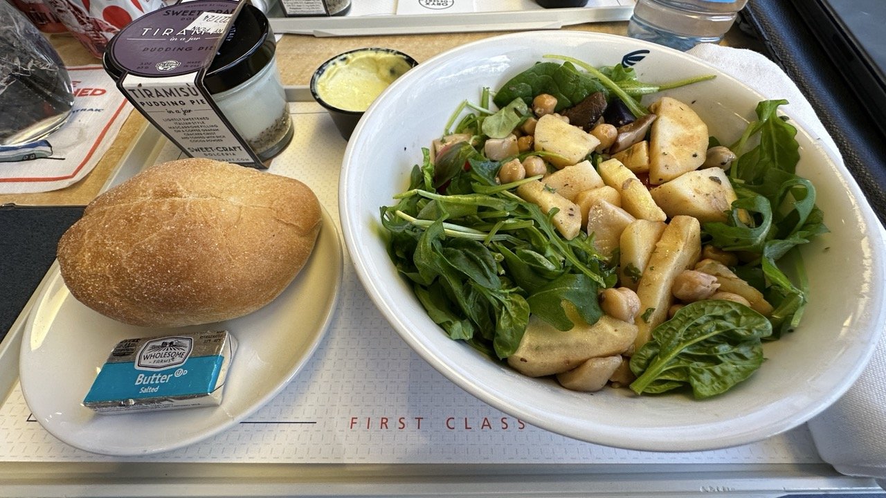 Amtrak first-class meal with a salad of roasted vegetables and chickpeas, a bread roll with butter, and a tiramisu dessert in a jar.