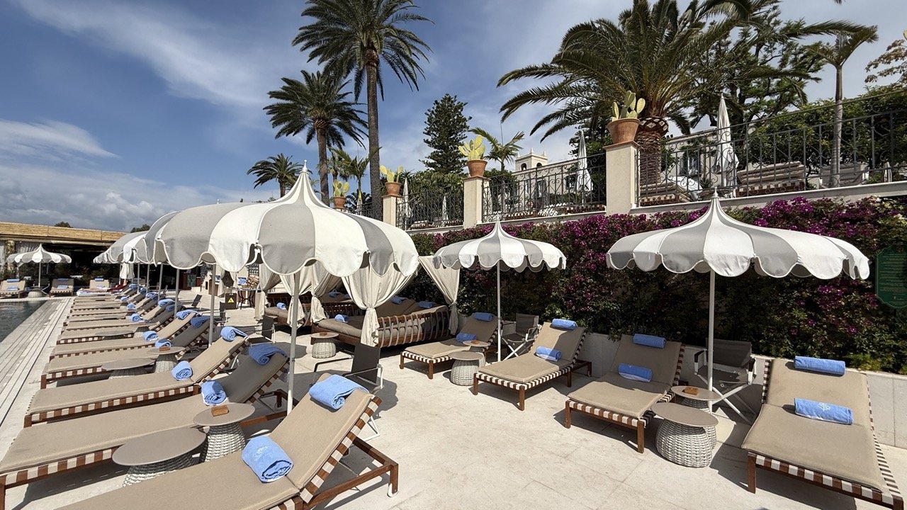 Lower pool terrace with loungers and parasols at Four Seasons Taormina surrounded by palms