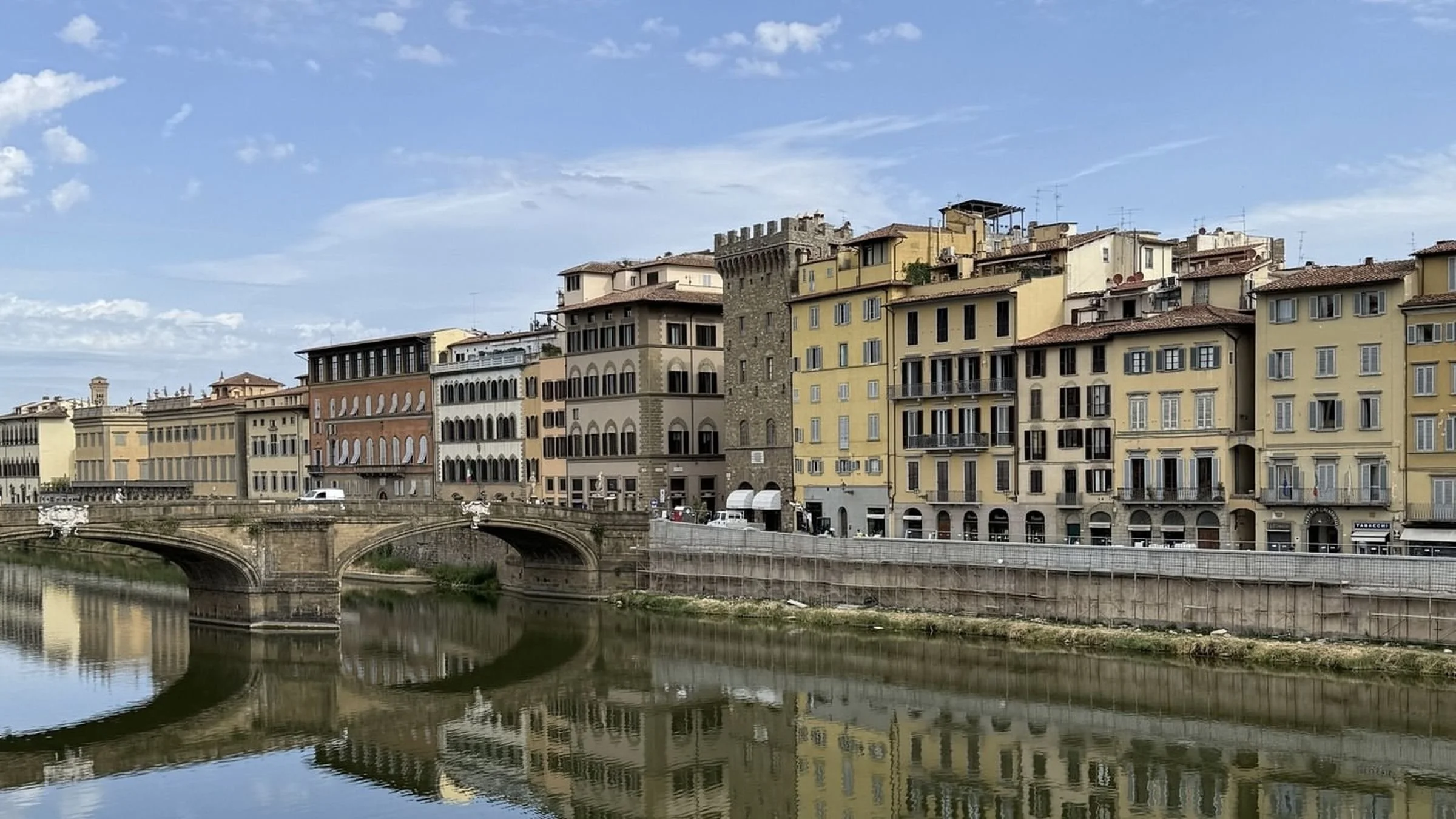 Historic buildings lining the Arno River in Florence, Italy, with elegant bridges and reflections across the water on a summer evening.