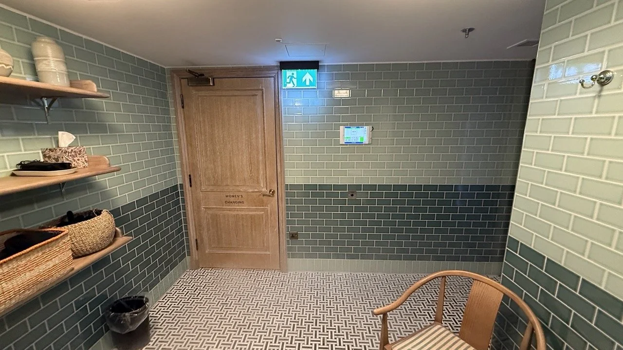 The women’s changing area at The Strong Rooms, featuring green subway tiles, wooden doors, and stylish shelving.