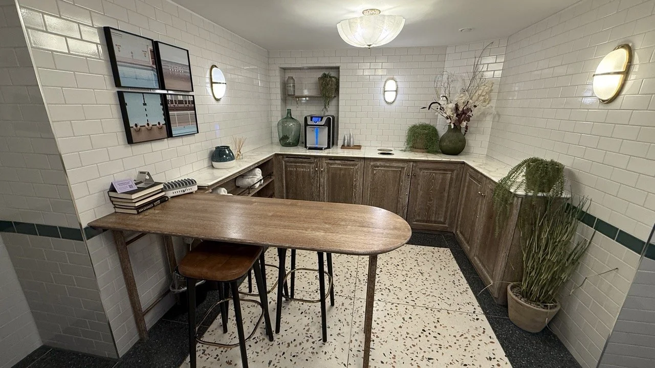 A stylish spa lounge at The Strong Rooms, featuring a wooden table, books, and a white subway-tiled refreshment station.