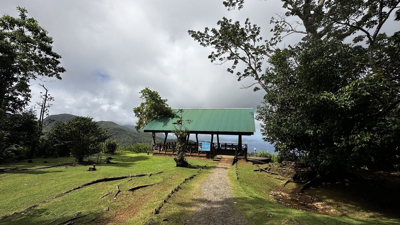 A small pavilion with a green roof located at a scenic viewpoint in Venn’s Town, Seychelles, surrounded by lush greenery and mountains.