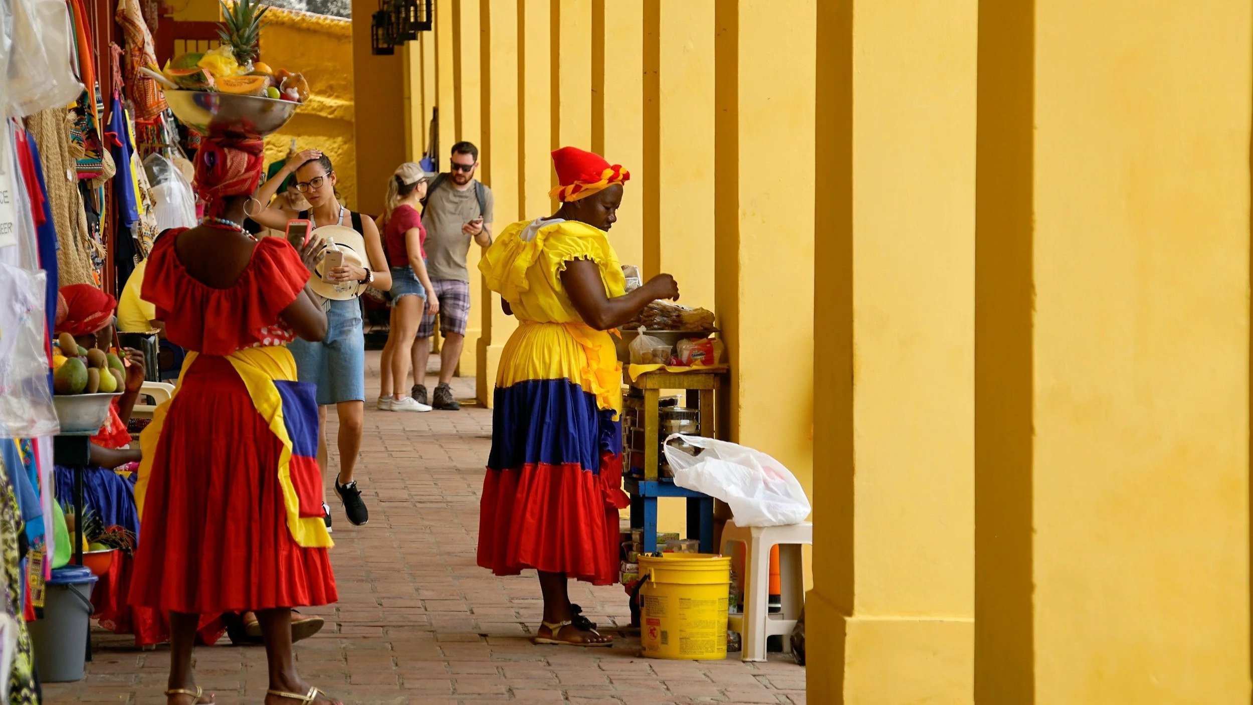 Palenquera women in traditional colourful dresses selling fruit along a colonnaded street in Cartagena Old Town, Colombia, captured during a luxury Colombia itinerary.