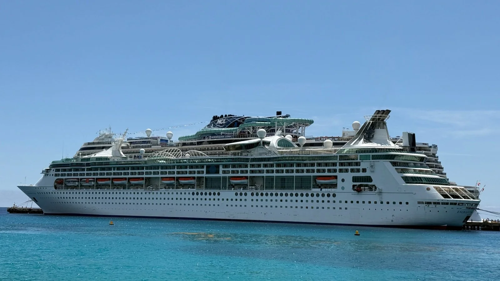 Large cruise ship docked in a Caribbean port with clear blue water and open ocean backdrop