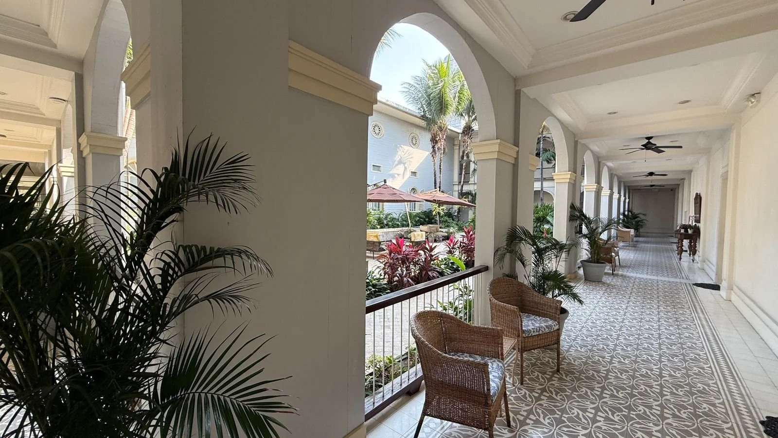 Arched colonial corridor with patterned tiles, wicker seating and views over a tropical courtyard