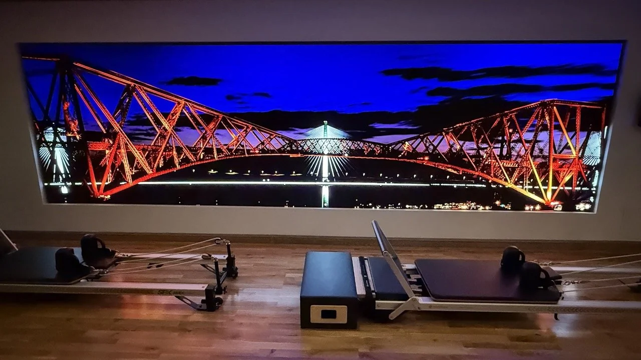 A modern Pilates studio at The Strong Rooms, featuring reformer machines and a striking mural of the Forth Bridge at night.