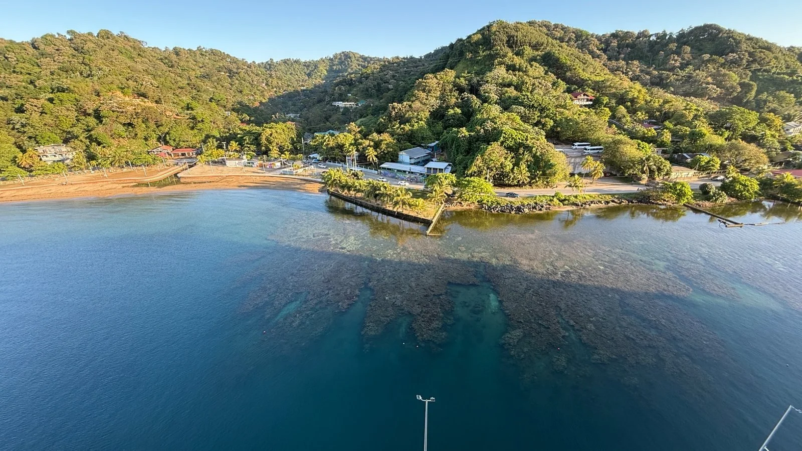 Aerial view of Roatán coastline in Honduras showing clear Caribbean waters, coral reef patterns and lush green hillside