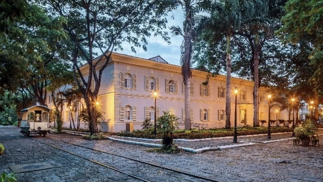 Exterior of Hotel del Parque in Guayaquil at dusk, a restored historic building set among trees with warm lighting and heritage railway tracks in the foreground