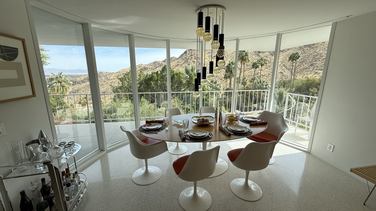 Elegant mid-century modern dining room at the Griffing House in Palm Springs, featuring tulip chairs, a statement chandelier, and stunning mountain views.