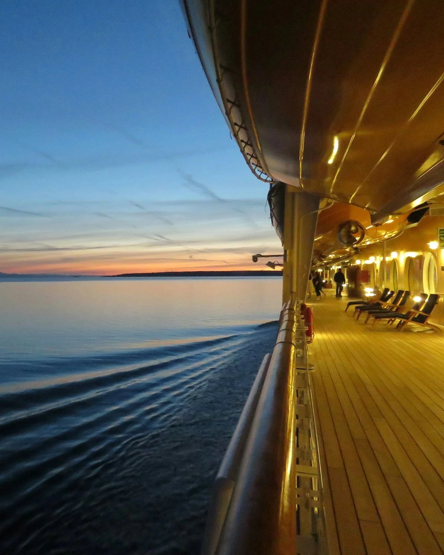 Sunset view from the promenade deck of a luxury cruise ship at sea, with golden evening light and calm ocean