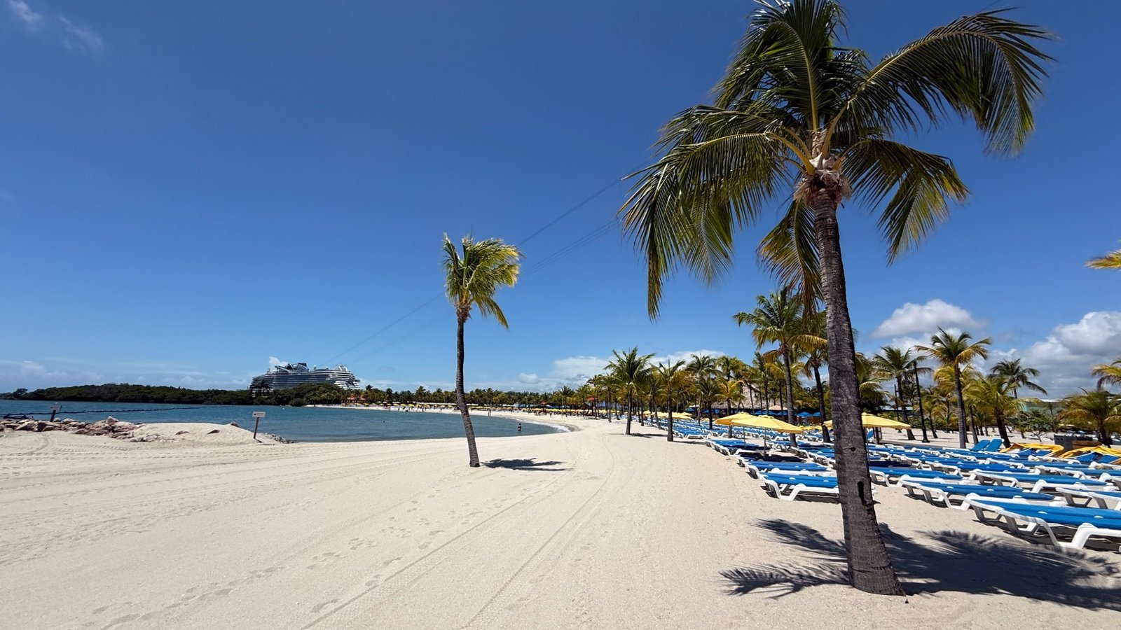 Palm-lined beach in Belize with sun loungers and a cruise ship anchored offshore in the Caribbean